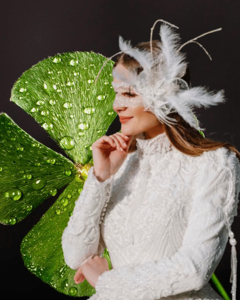 A woman gazes mysteriously to the side, wearing a white feather mask and an elegant white dress, set against a black background with a four-leaf clover