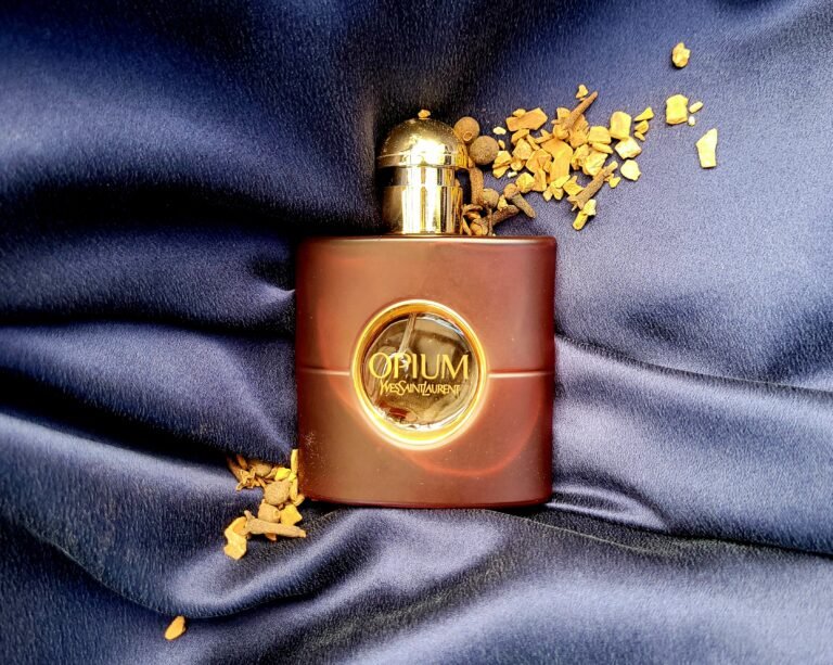 Yves Saint Laurent Opium perfume in a brick-red bottle, surrounded by autumn spices on a blue silk background.